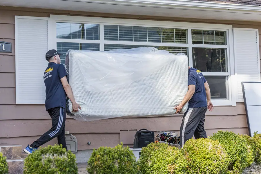Two movers carrying a wrapped mattress